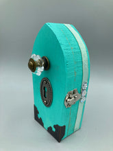 Load image into Gallery viewer, This Whimsical Fairy Wood Coffin Box is a truly unique and magical piece of home decor. With its vibrant turquoise exterior and eye-catching mini door knob, this Steampunk-inspired box is sure to be a conversation starter. Inside, the glittery gold interior and colorful butterfly detailing will bring a touch of fantasy to any room. The silver key and accompanying iridescent crystals complete the mystical and pastel goth look!