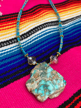 Load image into Gallery viewer, This vibrant and striking double strand necklace features a combination of glass beads in blue and green shades of turquoise, gold and champagne. The two delicate strands are accented with a gold-tone flower-shaped bead, a howlite stone chip dyed in turquoise, and shimmery, cross-faceted champagne-colored glass beads to complete the dramatic look. Measurements: Necklace is 17” and can be adjusted up to 19"