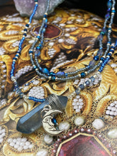 Load image into Gallery viewer, This jewelry piece is a delicate harmony of light and dark tones. Three strands feature a mix of navy blue, pewter, and oval-shaped, light blue-gray beads with a subtle iridescence of amethyst, emerald, and gold. Its celestial theme and bold composition create an alluringly elegant accessory. This whimsical necklace boasts a wonderfully unique aesthetic, featuring a wired blue luster nugget and a whimsical crescent moon charm. Measurements: Necklace is 15 1/4”adjustable up to 18"