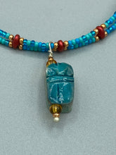 Load image into Gallery viewer, This adjustable choker style necklace features an eye-catching teal wood scarab beetle pendant and glass beaded strands. This dramatic necklace is kept together by double-hole flat matte lava-red beads, providing a collar shape. The necklace artfully wraps around the neck, conveying an elegant and bold style.  Measurements:    Necklace is 14 1/2” in length, can be adjusted up to 16"