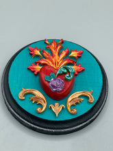 Load image into Gallery viewer, This Sacred Heart Wall Art Decor is the perfect way to enhance your home with an artistic flair. This beautiful artwork features a round bright turquoise wooden frame with a hand-crafted bright red heart. The heart is detailed with light purple and vibrant green leaves, with a vibrant fire embellishment over the center. Gold decorative embellishments at the sides of the heart add a luxurious touch. Diameter 4"