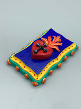 Load image into Gallery viewer, This Sacred Heart Wall Art Decor is the perfect way to enhance your home with an artistic flair. This Sacred Heart Wall Art Decor is crafted with a stunning red heart detailed with a black-silver cross and a vibrant fire embellishment at its center. Adding to its unique traditional Mexican aesthetic, the wood frame is decorated with marigold flowers, creating a beautiful and eye-catching artwork.