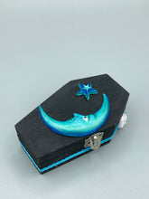Load image into Gallery viewer, This sleek black box has an eye-catching turquoise crescent at its center, accompanied by a bright blue ribbon and a dainty white moon. Inside, the interior is decorated with a vivid royal blue and detailed with a small crescent moon and black-and-silver cross. Coffin Dimensions: Length: 4 1/2 Inches; Width: 2 1/2 inches; Height: 1 5/8 Inches