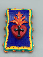 Load image into Gallery viewer, This Sacred Heart Wall Art Decor is the perfect way to enhance your home with an artistic flair. This Sacred Heart Wall Art Decor is crafted with a stunning red heart detailed with a black-silver cross and a vibrant fire embellishment at its center. Adding to its unique traditional Mexican aesthetic, the wood frame is decorated with marigold flowers, creating a beautiful and eye-catching artwork.