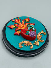 Load image into Gallery viewer, This Sacred Heart Wall Art Decor is the perfect way to enhance your home with an artistic flair. This beautiful artwork features a round bright turquoise wooden frame with a hand-crafted bright red heart. The heart is detailed with light purple and vibrant green leaves, with a vibrant fire embellishment over the center. Gold decorative embellishments at the sides of the heart add a luxurious touch. Diameter 4"