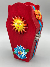 Load image into Gallery viewer, This coffin-shaped box features a bright red exterior, with a bold yellow, orange and red sun adorning the center. Complemented with a shimmery turquoise-blue ribbon and flower, the inside is painted in a dark royal blue hue with turquoise crescent moon detailing and traditional Mexican-themed fabric. Coffin Dimensions: Length: 4 1/2 Inches; Width: 2 1/2 inches; Height: 1 5/8 Inches