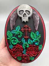 Load image into Gallery viewer, This Memento Mori Wall Art Decor is a one-of-a-kind art piece, skillfully crafted with a black polymer clay skull and wings on a dark red wood frame, decoratively woven with dark red roses and vines. It's perfect for adding an eye-catching touch to any wall and makes a unique, bold gift.  Measurements: H 7" x W 5” x D 1 1/2"
