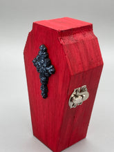 Load image into Gallery viewer, This unique ring box is sure to make an impression, with its simple but vibrant red coffin design and eye-catching black and gray floral cross in the center. The interior is black with a detailed fleur de lis, making the perfect resting place for your voodoo doll. It's spooky but also cute, with its accompanying Misfit VooDoo Doll.