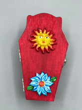 Load image into Gallery viewer, This coffin-shaped box features a bright red exterior, with a bold yellow, orange and red sun adorning the center. Complemented with a shimmery turquoise-blue ribbon and flower, the inside is painted in a dark royal blue hue with turquoise crescent moon detailing and traditional Mexican-themed fabric. Coffin Dimensions: Length: 4 1/2 Inches; Width: 2 1/2 inches; Height: 1 5/8 Inches