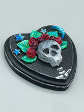 Load image into Gallery viewer, Showcasing a dark theme Frida Kahlo inspired calavera with a dark wood frame, this Day of the Dead wall decor piece is perfect for adding a traditional Mexican folk art touch to any home. Featuring an intricately detailed clay calavera in the style of Frida Kahlo, this Day of the Dead wall art decor is sure to be the centerpiece of any home décor. The calavera is wearing Frida's iconic crown of flowers, ensuring it will bring both a unique and inspiring look to any wall.