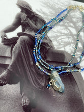 Load image into Gallery viewer, This jewelry piece is a delicate harmony of light and dark tones. Three strands feature a mix of navy blue, pewter, and oval-shaped, light blue-gray beads with a subtle iridescence of amethyst, emerald, and gold. Its celestial theme and bold composition create an alluringly elegant accessory. This whimsical necklace boasts a wonderfully unique aesthetic, featuring a wired blue luster nugget and a whimsical crescent moon charm. Measurements: Necklace is 15 1/4”adjustable up to 18"