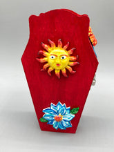 Load image into Gallery viewer, This coffin-shaped box features a bright red exterior, with a bold yellow, orange and red sun adorning the center. Complemented with a shimmery turquoise-blue ribbon and flower, the inside is painted in a dark royal blue hue with turquoise crescent moon detailing and traditional Mexican-themed fabric. Coffin Dimensions: Length: 4 1/2 Inches; Width: 2 1/2 inches; Height: 1 5/8 Inches
