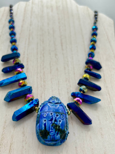 Powerful statement piece necklace features an eye-catching hand sculpted dark blue clay scarab beetle pendant. Adorned with vibrant sapphire luster quartz nuggets and sapphire faceted glass beaded necklace, this dramatic necklace artfully wraps around the neck, conveying an elegant and bold style. The Egyptian scarab symbol of rebirth, regeneration, and protection in the afterlife. Secure toggle clasp - Necklace is 23