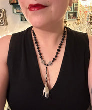 Load image into Gallery viewer, This sophisticated onyx beaded necklace features a large lucky hand charm adorned with floral metal beads, conveying an enchanting aura. The piece is finished with long black glass and floral metal beaded hanging strands, creating a bold and engaging visual statement. Measurements: Necklace: 19” in length - lucky hand charm is 4” Height

