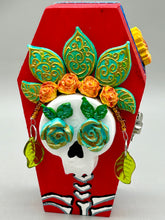 Load image into Gallery viewer, This coffin-shaped box features a bright and colorful exterior, showcasing a vibrant Frida Kahlo inspired calavera.  This beautifully handcrafted calavera is adorned with  Frida&#39;s iconic floral crown. To complete the look, the inside is also painted in colorful hues with a black and silver floral cross. The interior is also finished with a traditional Mexican-themed fabric.  L: 4 1/2“; W: 2 ½”; H: 1 5/8”
