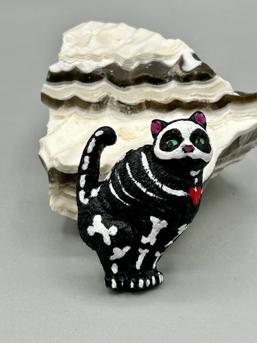 This hand-crafted art magnet featuring a skeleton cat is the ideal home decor for cat lovers, Halloween or Day Of The Dead enthusiasts. Perfect for adorning fridges, lockers, cubicles, and toolboxes.   I wanted to create an art piece that represented the eternal love for a special kitty cat in your life. Add a little touch of Mexican art to your home or office. This Day Of The Dead art was created for the cat lovers who adore their sweet kitty. H 2” x W 1/2” x D 3/8” 