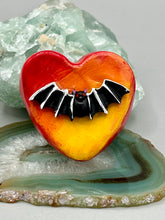 Load image into Gallery viewer, This hand-crafted art magnet is featuring a black bat with an ombre background of yellow, orange and bright red. This art clay magnet is the ideal home decor for Halloween enthusiasts. Perfect for adorning a witchy altar, goth, or spooky Halloween home decor.  Halloween magnet art to add to your fridge, locker, cubicle or toolbox. This hand-crafted heart-shaped magnet features a black bat figurine with ombre colors of yellow, orange and bright red.
