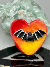 Load image into Gallery viewer, This hand-crafted art magnet is featuring a black bat with an ombre background of yellow, orange and bright red. This art clay magnet is the ideal home decor for Halloween enthusiasts. Perfect for adorning a witchy altar, goth, or spooky Halloween home decor.  Halloween magnet art to add to your fridge, locker, cubicle or toolbox. This hand-crafted heart-shaped magnet features a black bat figurine with ombre colors of yellow, orange and bright red.
