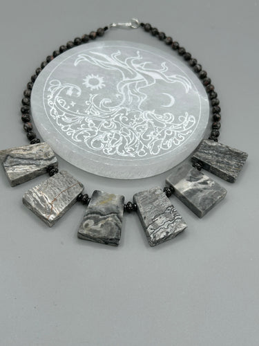 This rustic necklace features an eye-catching large trapezoid-shaped Picasso jasper and black agate combo set in a unique and chic design. Handcrafted from genuine stones, this necklace is perfect for any bohemian look.   Measurements:  Necklace is 19 1/2