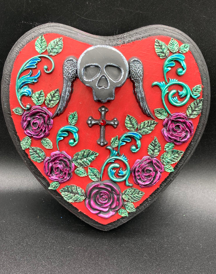 Memento Mori Wall Art Decor is crafted with a black polymer clay skull and wings on a dark red wood frame, decoratively woven with dark red roses and vines. 