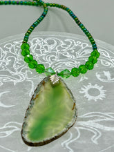 Load image into Gallery viewer, This Light Green Agate Geode Sliced Stone Chip Necklace is a statement piece for your jewelry collection. It features a bold green agate geode pendant surrounded by a glass bead necklace in varying shades of green. The silver leaf bail completes this chic, Boho-inspired necklace.  Measurements:   Necklace is 18” in length - pendant is 2 1/4” Height
