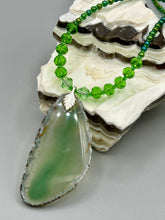 Load image into Gallery viewer, This Light Green Agate Geode Sliced Stone Chip Necklace is a statement piece for your jewelry collection. It features a bold green agate geode pendant surrounded by a glass bead necklace in varying shades of green. The silver leaf bail completes this chic, Boho-inspired necklace.  Measurements:   Necklace is 18” in length - pendant is 2 1/4” Height

