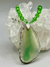 Load image into Gallery viewer, This Light Green Agate Geode Sliced Stone Chip Necklace is a statement piece for your jewelry collection. It features a bold green agate geode pendant surrounded by a glass bead necklace in varying shades of green. The silver leaf bail completes this chic, Boho-inspired necklace.  Measurements:   Necklace is 18” in length - pendant is 2 1/4” Height
