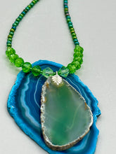 Load image into Gallery viewer, This Light Green Agate Geode Sliced Stone Chip Necklace is a statement piece for your jewelry collection. It features a bold green agate geode pendant surrounded by a glass bead necklace in varying shades of green. The silver leaf bail completes this chic, Boho-inspired necklace.  Measurements:   Necklace is 18” in length - pendant is 2 1/4” Height
