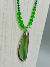 Load image into Gallery viewer, This Light Green Agate Geode Sliced Stone Chip Necklace is a statement piece for your jewelry collection. It features a bold green agate geode pendant surrounded by a glass bead necklace in varying shades of green. The silver leaf bail completes this chic, Boho-inspired necklace.  Measurements:   Necklace is 18” in length - pendant is 2 1/4” Height

