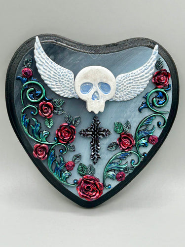 This Memento Mori Wall Art Decor is a one-of-a-kind art piece, skillfully crafted with a polymer clay skull and wings on a dark gray hear shape wood frame, decoratively woven with dark red roses and vines. It's perfect for adding an eye-catching touch to any wall and makes a unique, bold gift. W 6 1/2