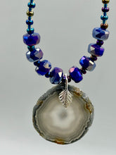 Load image into Gallery viewer, This Dark Gray-blue Agate Geode Sliced Stone Chip Necklace is a unique, eye-catching accessory to elevate your jewelry collection. The bold pendant features a striking gray-blue agate geode surrounded by eye-catching, shimmery dark-purple glass beads with beautiful iridescence that reflects hues of blue, pink, gold, and green. It&#39;s a perfect boho chic accent to update any look.   Measurements:   Necklace is 18” in length - pendant is 1 1/4” Height
