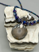 Load image into Gallery viewer, This Dark Gray-blue Agate Geode Sliced Stone Chip Necklace is a unique, eye-catching accessory to elevate your jewelry collection. The bold pendant features a striking gray-blue agate geode surrounded by eye-catching, shimmery dark-purple glass beads with beautiful iridescence that reflects hues of blue, pink, gold, and green. It&#39;s a perfect boho chic accent to update any look.   Measurements:   Necklace is 18” in length - pendant is 1 1/4” Height
