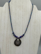 Load image into Gallery viewer, This Dark Gray-blue Agate Geode Sliced Stone Chip Necklace is a unique, eye-catching accessory to elevate your jewelry collection. The bold pendant features a striking gray-blue agate geode surrounded by eye-catching, shimmery dark-purple glass beads with beautiful iridescence that reflects hues of blue, pink, gold, and green. It&#39;s a perfect boho chic accent to update any look.   Measurements:   Necklace is 18” in length - pendant is 1 1/4” Height
