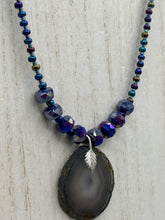 Load image into Gallery viewer, This Dark Gray-blue Agate Geode Sliced Stone Chip Necklace is a unique, eye-catching accessory to elevate your jewelry collection. The bold pendant features a striking gray-blue agate geode surrounded by eye-catching, shimmery dark-purple glass beads with beautiful iridescence that reflects hues of blue, pink, gold, and green. It&#39;s a perfect boho chic accent to update any look.   Measurements:   Necklace is 18” in length - pendant is 1 1/4” Height
