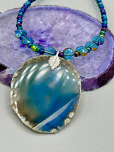 Load image into Gallery viewer, This Dark Blue Agate Geode Sliced Stone Chip Necklace is a luxurious addition to any jewelry collection. It features bold, eye-catching dark blue agate geode in an earthy outline, suspended on a unique glass beaded necklace that contains a mixture of blue and purple glass beads with a beautiful iridescence. This necklace is the perfect boho chic accent to take any look to the next level.   Measurements:    Necklace is 18” in length - pendant is 1 3/4” Height
