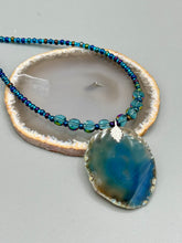 Load image into Gallery viewer, This Dark Blue Agate Geode Sliced Stone Chip Necklace is a luxurious addition to any jewelry collection. It features bold, eye-catching dark blue agate geode in an earthy outline, suspended on a unique glass beaded necklace that contains a mixture of blue and purple glass beads with a beautiful iridescence. This necklace is the perfect boho chic accent to take any look to the next level.   Measurements:    Necklace is 18” in length - pendant is 1 3/4” Height

