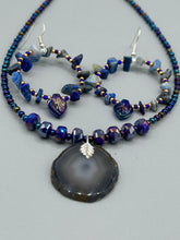 Load image into Gallery viewer, These Lapis Stone Chip Beaded Hoop Earrings feature a dark blue-tone pressed glass leaf charm with an iridescent shimmer finish showcasing hues of gold, purple, blue and pink. The earrings display natural lapis stone chips and royal blue with gold glass beads.  Measurements: 1 1/2&quot; length
