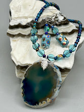 Load image into Gallery viewer, This set of glass beaded earrings features a vibrant blue shade with hints of purples and gold for an overall dynamic look. Its unique texture is derived from the combination of different size and shaped beads, resulting in a bold, eye-catching piece. For any discerning connoisseur, this set is a must-have addition to any jewelry collection.  Measurements: 1 1/2” in length
