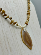 Load image into Gallery viewer, This Light Brown Banded Agate Geode Sliced Stone Chip Necklace is a luxurious addition to any jewelry collection. It features natural, light brown agate banded geode in a luxurious earth-tone. Suspended on a unique strand of natural bamboo chips and gold and clear beaded necklace. The combination of neutral colors and nature inspired design makes them the perfect accessory for any outfit.   Measurements:    Necklace is 18” in length - pendant is 2” Height

