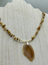 Load image into Gallery viewer, This Light Brown Banded Agate Geode Sliced Stone Chip Necklace is a luxurious addition to any jewelry collection. It features natural, light brown agate banded geode in a luxurious earth-tone. Suspended on a unique strand of natural bamboo chips and gold and clear beaded necklace. The combination of neutral colors and nature inspired design makes them the perfect accessory for any outfit.   Measurements:    Necklace is 18” in length - pendant is 2” Height
