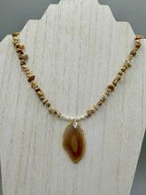 Load image into Gallery viewer, This Light Brown Banded Agate Geode Sliced Stone Chip Necklace is a luxurious addition to any jewelry collection. It features natural, light brown agate banded geode in a luxurious earth-tone. Suspended on a unique strand of natural bamboo chips and gold and clear beaded necklace. The combination of neutral colors and nature inspired design makes them the perfect accessory for any outfit.   Measurements:    Necklace is 18” in length - pendant is 2” Height
