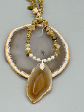 Load image into Gallery viewer, This Light Brown Banded Agate Geode Sliced Stone Chip Necklace is a luxurious addition to any jewelry collection. It features natural, light brown agate banded geode in a luxurious earth-tone. Suspended on a unique strand of natural bamboo chips and gold and clear beaded necklace. The combination of neutral colors and nature inspired design makes them the perfect accessory for any outfit.   Measurements:    Necklace is 18” in length - pendant is 2” Height
