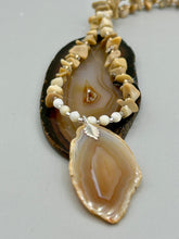 Load image into Gallery viewer, This Light Brown Banded Agate Geode Sliced Stone Chip Necklace is a luxurious addition to any jewelry collection. It features natural, light brown agate banded geode in a luxurious earth-tone. Suspended on a unique strand of natural bamboo chips and gold and clear beaded necklace. The combination of neutral colors and nature inspired design makes them the perfect accessory for any outfit.   Measurements:    Necklace is 18” in length - pendant is 2” Height
