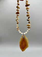 Load image into Gallery viewer, This Light Brown Banded Agate Geode Sliced Stone Chip Necklace is a luxurious addition to any jewelry collection. It features natural, light brown agate banded geode in a luxurious earth-tone. Suspended on a unique strand of natural bamboo chips and gold and clear beaded necklace. The combination of neutral colors and nature inspired design makes them the perfect accessory for any outfit.   Measurements:    Necklace is 18” in length - pendant is 2” Height

