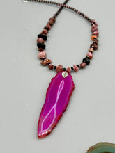 Load image into Gallery viewer, Unlock your inner goddess with this stunning Large Fuchsia Agate Geode Sliced Stone Chip Necklace. Featuring a vibrant fuchsia agate geode pendant surrounded by Rhodonite stone chips and gold and black glass beading, the silver leaf bail completes this chic and boho-inspired look. Make a bold statement with this bohemian-style gemstone necklace.   Measurements:    Necklace is 17 3/4” in length - pendant is 3” Height
