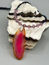 Load image into Gallery viewer, Make a bold style statement with this eye-catching Soft Pink and Amber Agate Geode Sliced Stone Chip Necklace. Featuring a vibrant soft pink and amber tone agate geode pendant surrounded by dark blue glass beads with iridescent tones of purple, blue, green, pink and gold. This bohemian-style gemstone necklace is the perfect way to add a unique touch of shabby boho chic to any look.   Measurements:    Necklace is 18” in length - pendant is 2 1/4” Height
