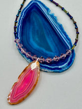 Load image into Gallery viewer, Make a bold style statement with this eye-catching Soft Pink and Amber Agate Geode Sliced Stone Chip Necklace. Featuring a vibrant soft pink and amber tone agate geode pendant surrounded by dark blue glass beads with iridescent tones of purple, blue, green, pink and gold. This bohemian-style gemstone necklace is the perfect way to add a unique touch of shabby boho chic to any look.   Measurements:    Necklace is 18” in length - pendant is 2 1/4” Height
