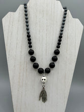 Load image into Gallery viewer, This elegant Peruvian ceramic skull beaded necklace is the perfect accessory for your unique look. With a large skull bead and a lucky hand charm, it exudes a dark, alluring vibe. Complemented with black glass and hematite stone beads, it will make a bold statement. Measurements:  Necklace: 19” in length - skulls with lucky hand charm is 2 3/4” Height
