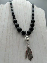 Load image into Gallery viewer, This elegant Peruvian ceramic skull beaded necklace is the perfect accessory for your unique look. With a large skull bead and a lucky hand charm, it exudes a dark, alluring vibe. Complemented with black glass and hematite stone beads, it will make a bold statement. Measurements:  Necklace: 19” in length - skulls with lucky hand charm is 2 3/4” Height
