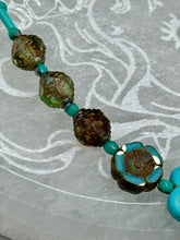 Load image into Gallery viewer, Adorn your look and show your affinity for nature with this exquisite handcrafted necklace, composed of a large intricate sea-green hibiscus pressed glass bead, a lucky hand charm, multiple turquoise, and dark avocado green faceted pressed glass beads, and a hook-eye clasp for secure wear. This nature-inspired statement piece brings warmth to any outfit for both day and night. Measurements:  Necklace: 19 1/2&quot;, Flower and lucky hand pendant 3&quot;
